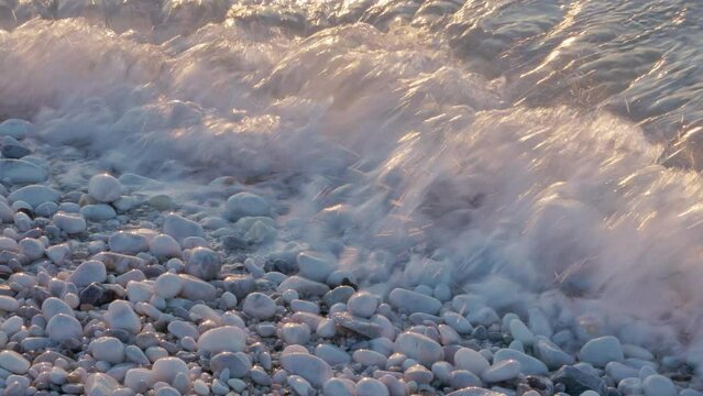 Closeup of ocean waves on white pebbles beach at sunset. 4K, 30 fps, h265, 4:2:2 10 bit.