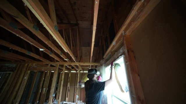 Woman pulls fiberglass insulation out of walls and ceiling in a residential or commercial demolition preparing for a renovation.