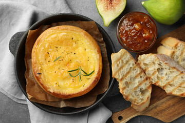 Tasty baked brie cheese and products on grey table, flat lay
