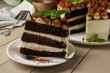 Piece of delicious tiramisu cake with mint leaves on wooden table, closeup
