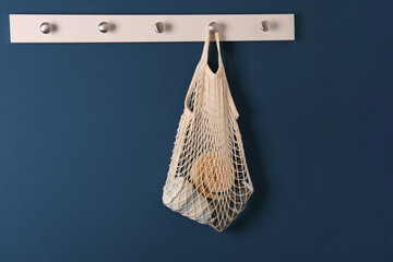 Conscious consumption. Net bag with eco friendly products hanging on blue wall indoors, space for...
