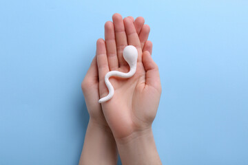 Reproductive medicine. Woman holding figure of sperm cell on light blue background, top view - obrazy, fototapety, plakaty