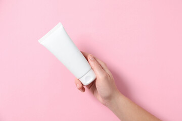 Woman with tube of hand cream on pink background, top view