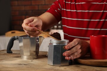 Man putting ground coffee into moka pot at wooden table indoors, closeup