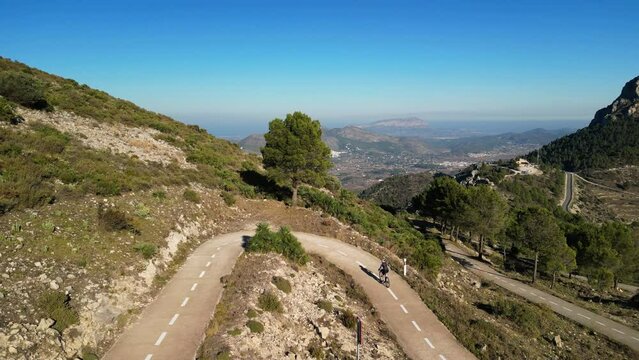 A woman cyclist engaging in an intense cycling workout. Cycling and triathlon concept. Professional female cyclist speeding up on her bicycle on the mountain hill Coll de Rates in Spain.