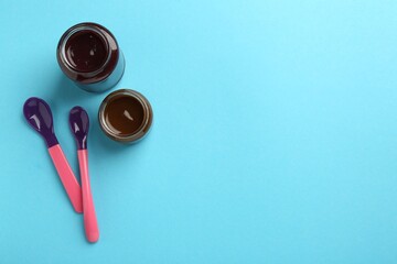 Jars with healthy baby food and spoons on light blue background, flat lay. Space for text