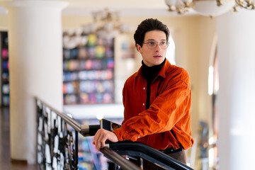 portrait of a young guy in glasses standing with a book in his hands in the library