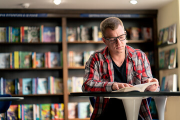 male professor in glasses sits in a scientific and technical library reads a book and prepares to...