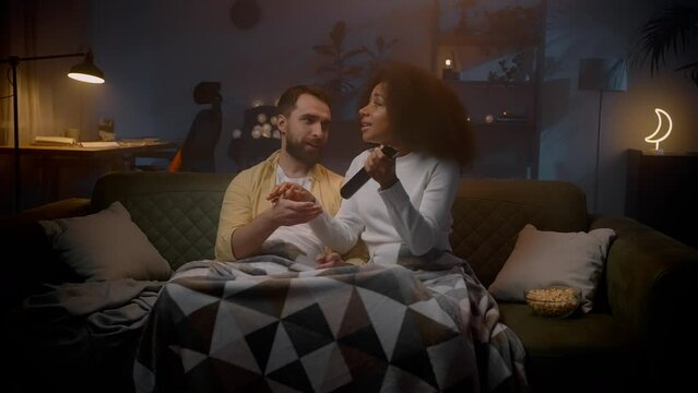 Emotional multiracial pair enjoying tv fighting for remote controller at evening together
