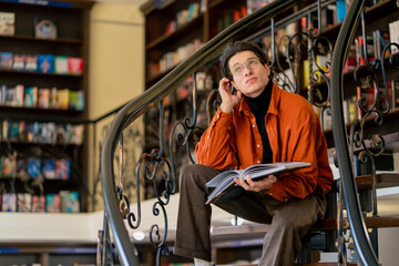 guy in glasses sits on the stairs and reads a book enthusiastically shocked by the plot of the...