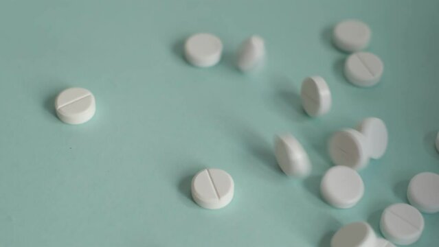 Scattered white pills on a teal background, depicting pharmaceutical care and health management. A random arrangement of medication tablets, a representation of modern medical treatments.