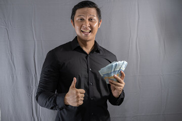 Young Asian businessman holding money with a happy gesture because his business and finances are on...
