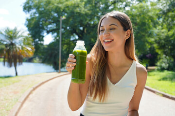 Portrait of healthy woman holding a bottle of green smoothie detox juice homemade outdoors. Looking...