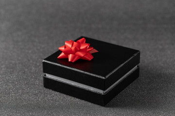 Black gift box with red bow on blurred dark silver glitter background.
