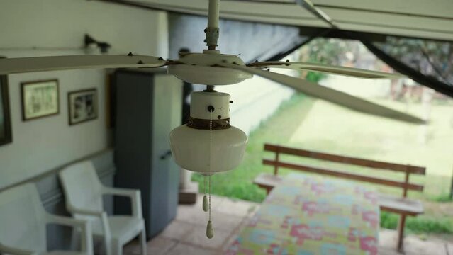 Person hand turning on ceiling fan pulling chain down, old electric ceiling ventilator speeding up, rotating blades and cooling air. Electric ceiling fan with lamp being a part of house interior decor