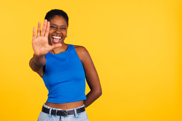 Portrait of a cheerful young beautiful woman wearing blue clothes standing against a yellow background. Young woman looking at the camera.