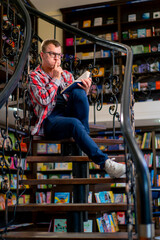 a man in glasses sits on the stairs in the library carefully reads a book and worries for its...