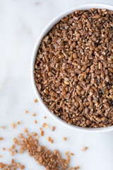 Close up of wheat grains in bowl on marble background. Healthy food concept.