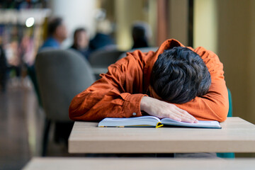 tired boy student sleeping in front of a book in the library after preparing for university exams