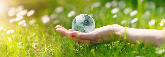 Woman hands holding a glass sphere of Earth on the green grass background.