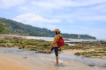 Tourists walk along the beach on vacation. Women use their bare feet to kick sea water until it splashes with joy. The seaside atmosphere during the summer day can see the lighthouse in the distance.
