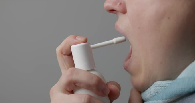 A woman with a sore throat sprays medicine aerosol spray down her throat