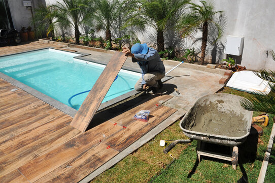 trabalhador acentando porcelanato em piso , passando argamassa no ch&atilde;o, acabamento de area externa de lazer 