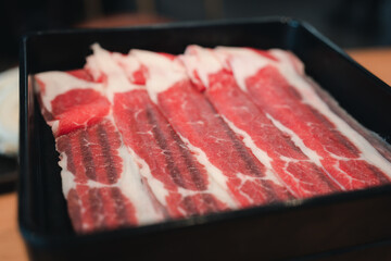 Thin beef slices for of raw thinly sliced beef served on black tray. Close up