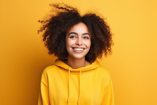 Excited smiling happy student girl young woman with curly hair in hoodie on isolated yellow background studio portrait. Positive people anouncement concept. Empty space place for text copy paste