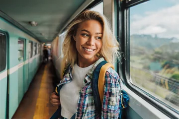 Fotobehang Junge lächelnde Frau mit blonden Haaren und Rucksack auf Reisen in einem Zug am Fenster © Tim B.