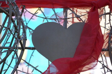 Metal silver-coloured heart hidden by metal rods and Christmas lights, partially covered with red, translucent, shimmering cloth