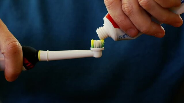 Man squeezing toothpaste from tube onto electric toothbrush closeup conceptual health and wellness dental hygiene