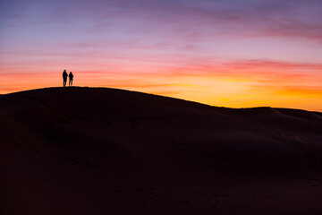 朝焼けの砂丘に立つカップルのシルエット