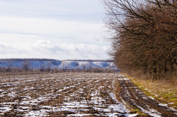 Plowed field under snow, black photo of rows of soil before sowing. furrows on arable land prepared...