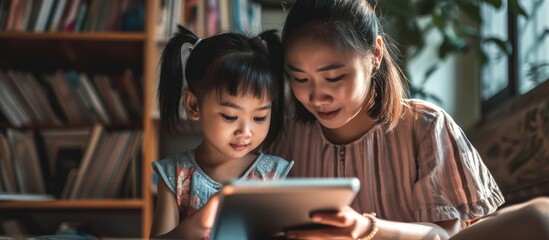 Young Asian girl and her mother using a tablet for e-Learning and attending online classes. - obrazy, fototapety, plakaty
