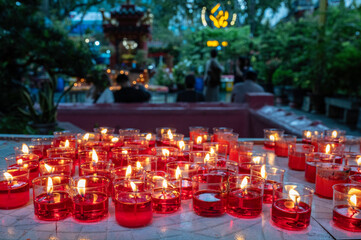Small, red candles, lit in a temple in south east Asia.  The focus is on the candles in the...