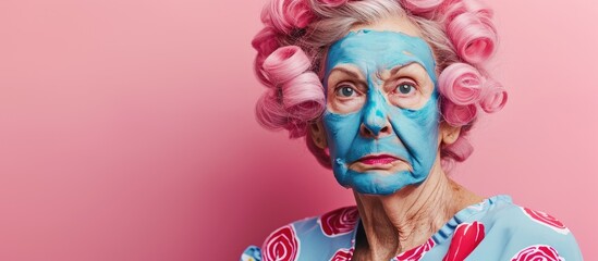 Elderly woman in pink curlers and blue hyaluronic mask getting ready for Valentine's Day date in studio.