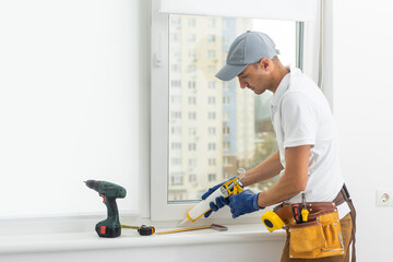 Using drill by installing windows. Repairman is working indoors in the modern room - obrazy, fototapety, plakaty