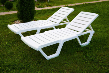 Empty white plastic chair or chaise longue, on the green grass of a fresh lawn. Recreation and tourism advertising.