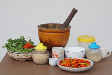 Wooden mortar,pestle, vegetables, plate of red chillies, glass jar of sugar, ceramic bowls and mugs. Concept,preparing food ingredient and equipment for cooking. Thai traditional cooking style.