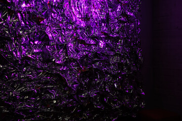 Vibrant purple and glowing abstract background. Illuminated crumpled foil. Defocused lights.