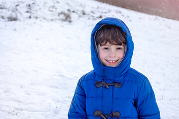 Portrait happy boy in warm winter clothesstanding on a snow covered field in sunny winter day. Concept representing winter childhood, leisure activities during the cold season, and family fun.