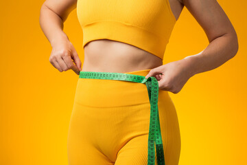 Fitness woman with measure tape isolated on yellow background. Weight loss and healthcare concept