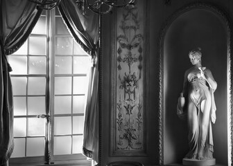 Elegant black and white photo of a classical statue by a window with flowing drapes. MET, NY. Ideal for themes of art, history, and sophistication in wall art, home décor, or educational materials.