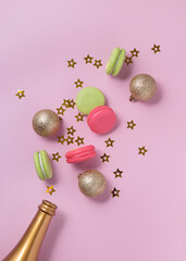 New Year celebration flatlay with golden champagne bottle, confetti stars, colorful macarons, gold Christmas decoration balls, pink background. Top view 