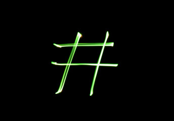 A photograph of a hashtag symbol in vibrant green light in a long exposure photo against a black...