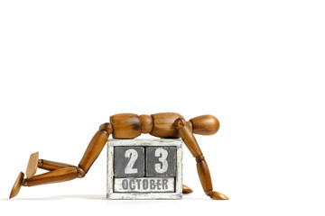 October 23, wooden calendar with mannequin lying on it on white background. Calendar date.