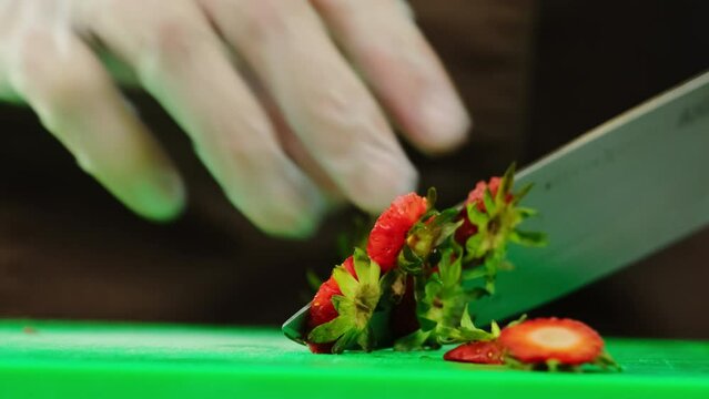 Man donning latex gloves adeptly removes strawberry stems using knife. Chef prioritizes cleaning berries before smoothie making