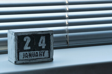 Morning January 24 on wooden calendar standing on window with blinds.