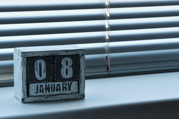 Morning January 08 on wooden calendar standing on window with blinds.